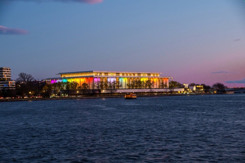 The Kennedy Center lit in colour at dusk, seen across the Potomac under a pink sky.
