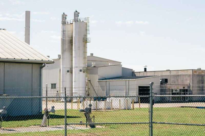A factory in Hamilton, Ohio, with metal silos and low industrial buildings behind a chain-link fence and a mown lawn.