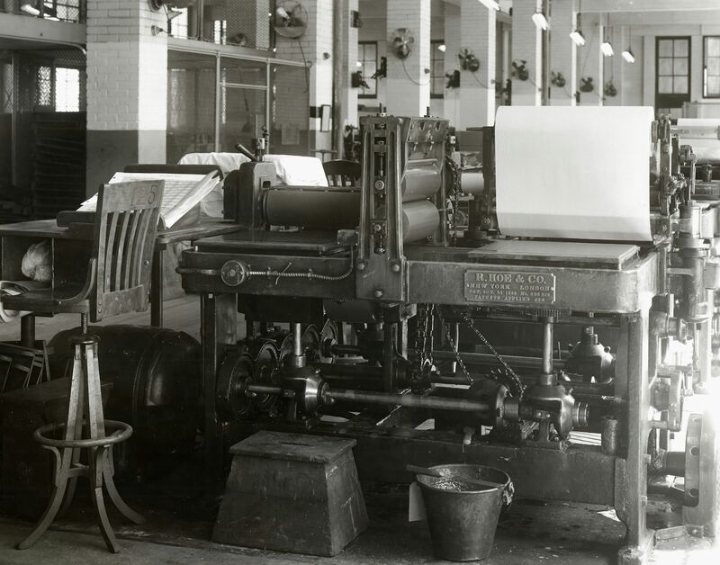 A vintage R. Hoe and Company printing press in a pressroom, photographed in black and white.