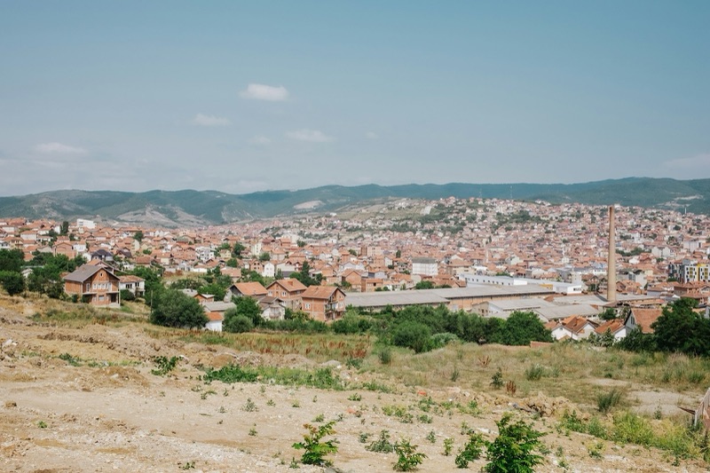 A view over the red roofs and hills of Pristina from a dirt slope on the city's edge.