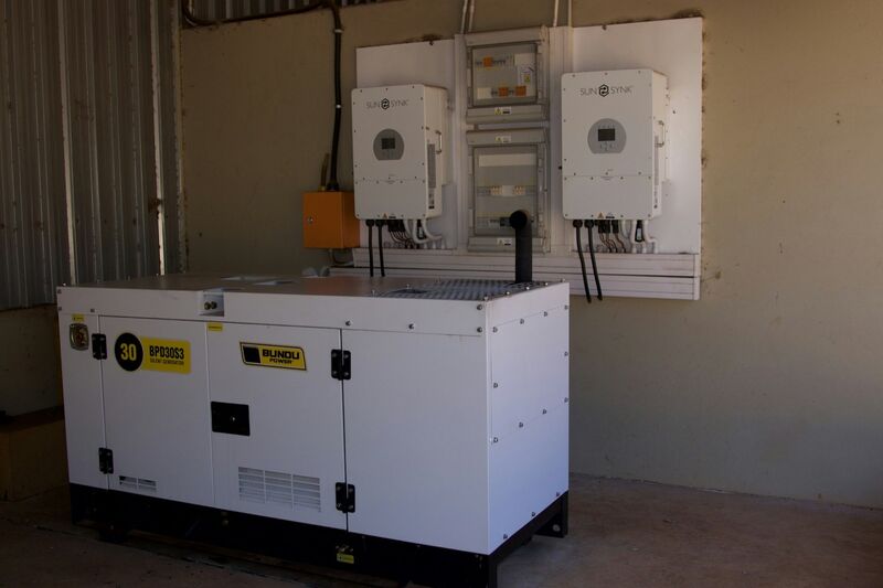 A white diesel generator in a utility room beneath wall-mounted electrical units.