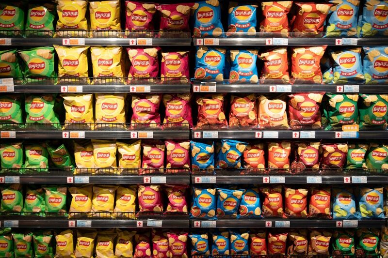 Rows of Lay's potato chip bags in yellow, pink, blue and green packaging on metal supermarket shelves, with Chinese-language labels and price tags.