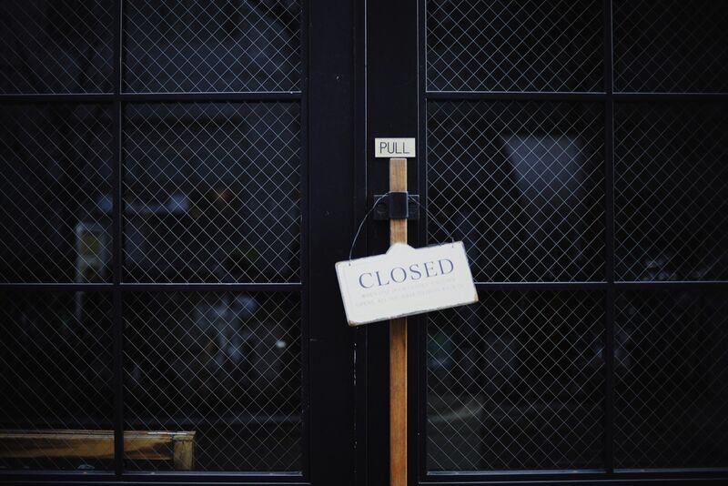 A black metal gate closed across an entrance, with a closed sign hanging on it.