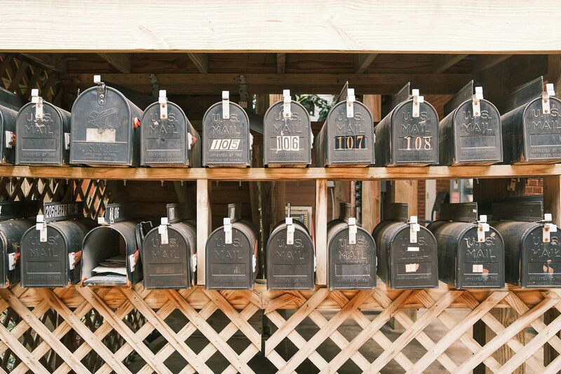 Rows of weathered black US Mail boxes on a wooden rack, several numbered, one hanging open with letters inside