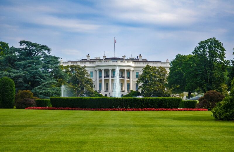The north front of the White House behind its lawn on a clear day.