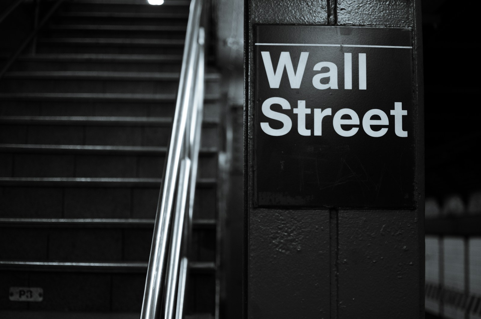 The Wall Street subway station sign beside an empty staircase, in black and white.