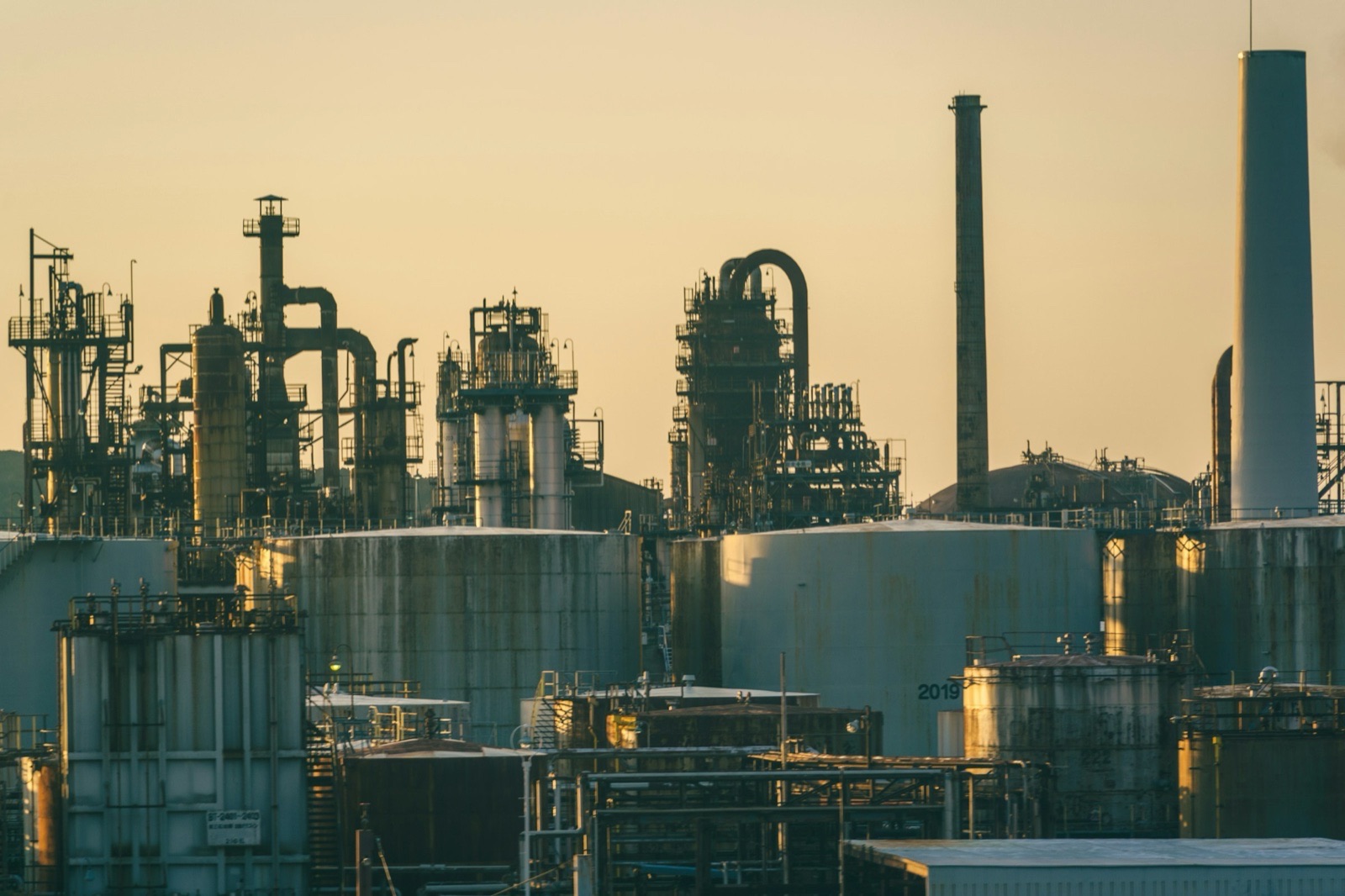 An oil refinery in Japan at dusk, with storage tanks, towers, pipework and chimneys silhouetted against a golden sky.
