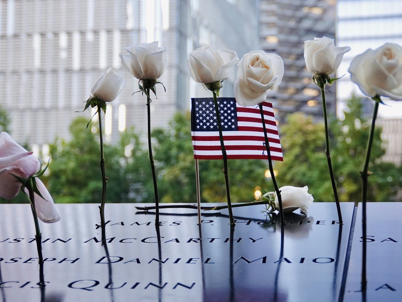White roses and a small American flag placed in the incised names on the bronze parapet of the September 11 Memorial.