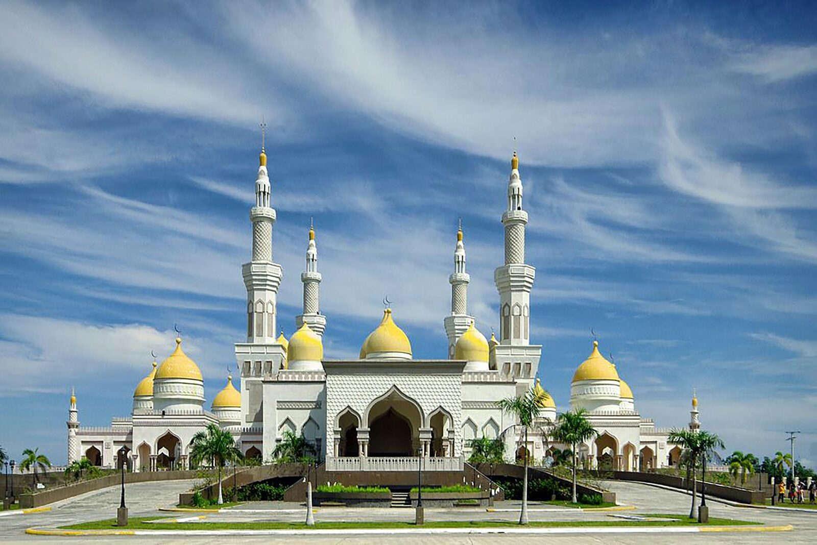 The white Grand Mosque in Cotabato City, with golden domes and tall minarets, under a blue sky.