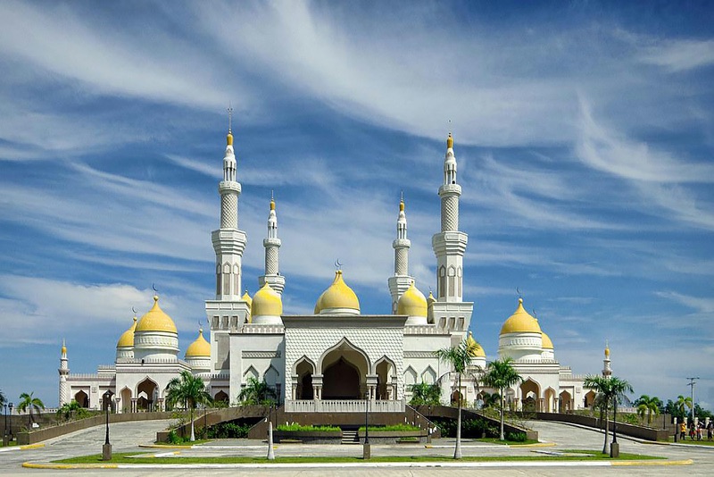 The white Grand Mosque in Cotabato City, with golden domes and tall minarets, under a blue sky.