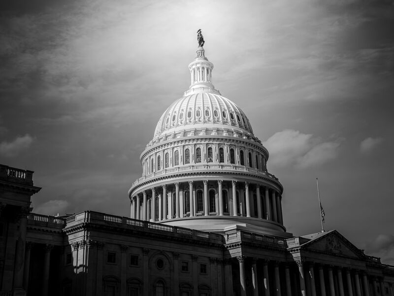 The dome of the United States Capitol in black and white against a dark, dramatic sky.