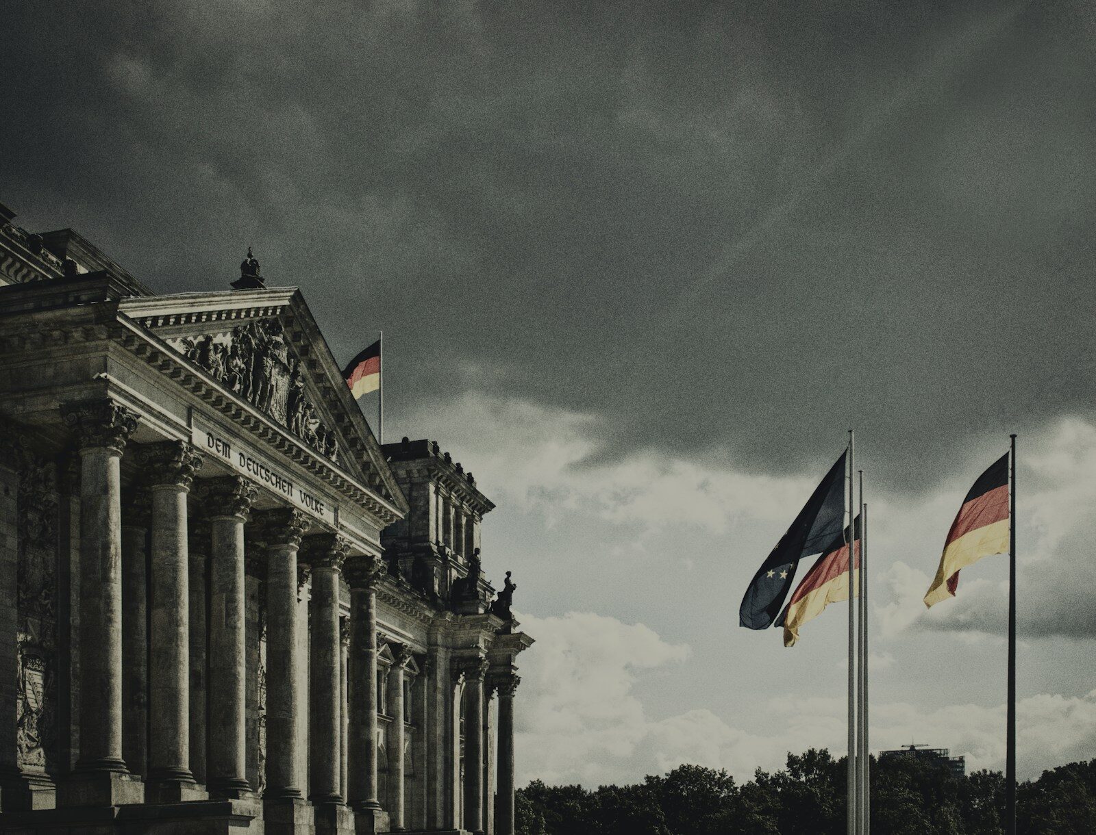The Reichstag in Berlin beneath a dark sky, with the German and European Union flags flying beside it.