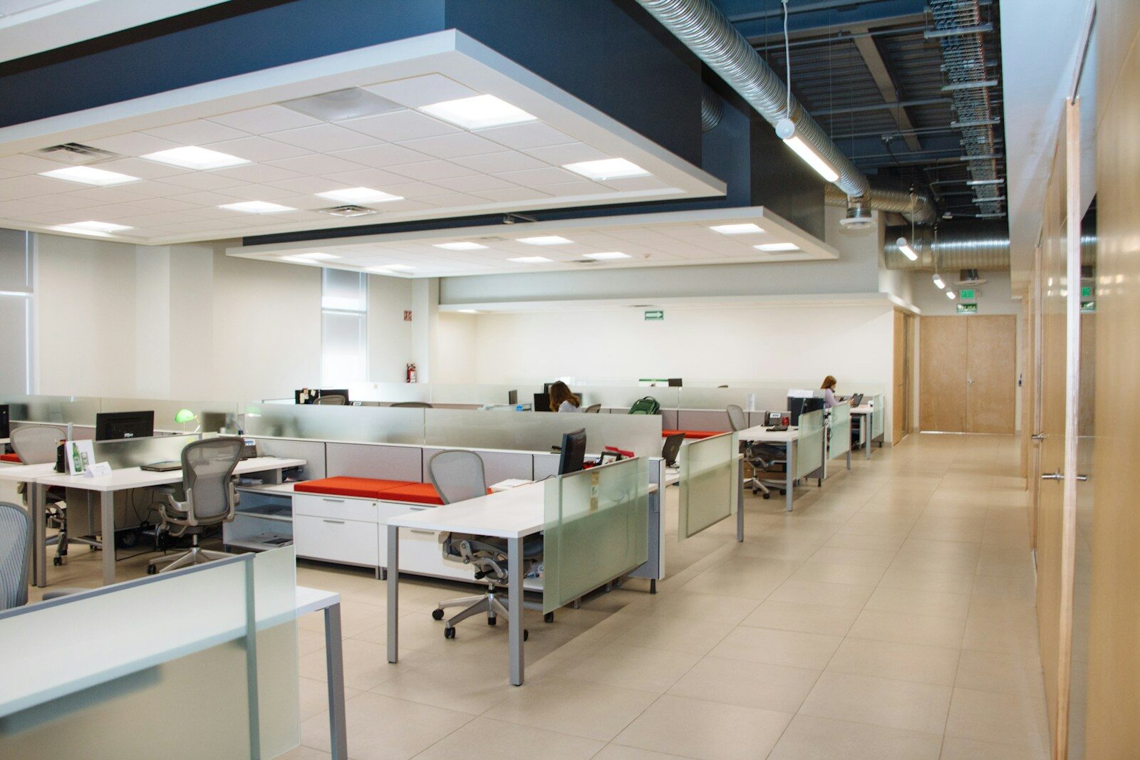 An open-plan office seen down a corridor, with rows of white desks behind frosted glass partitions and most of the chairs empty.