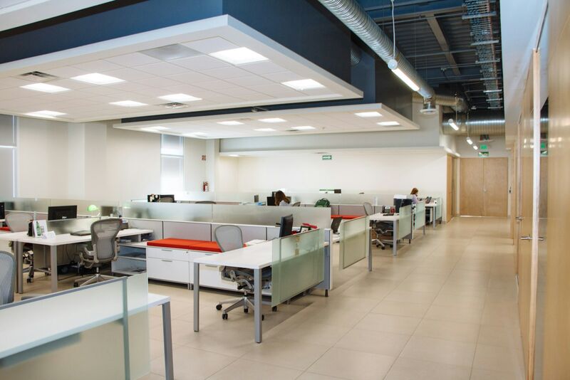 An open-plan office seen down a corridor, with rows of white desks behind frosted glass partitions and most of the chairs empty.