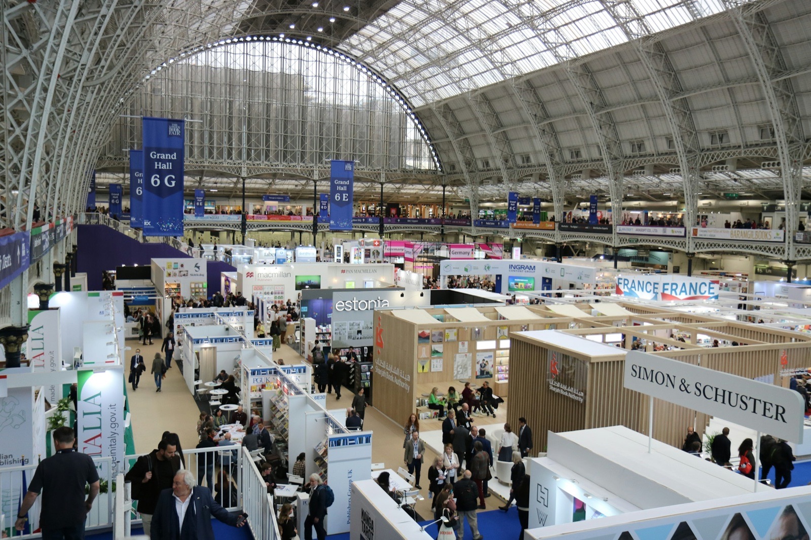 Publishers' stands and visitors beneath the arched glass roof of a large exhibition hall.