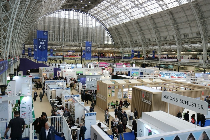Publishers' stands and visitors beneath the arched glass roof of a large exhibition hall.