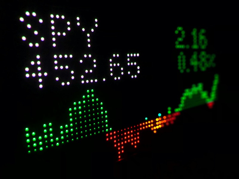 An LED stock ticker display in the dark showing the SPY symbol, a price of 452.65 and a red and green price chart.