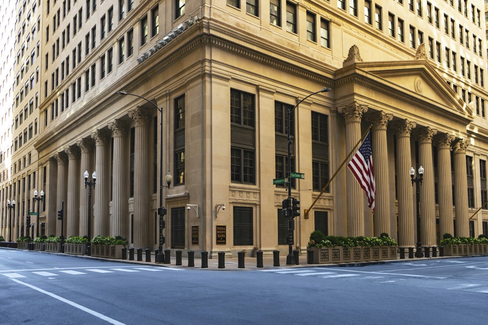 The columned stone facade of a Federal Reserve building with an American flag hanging at the corner