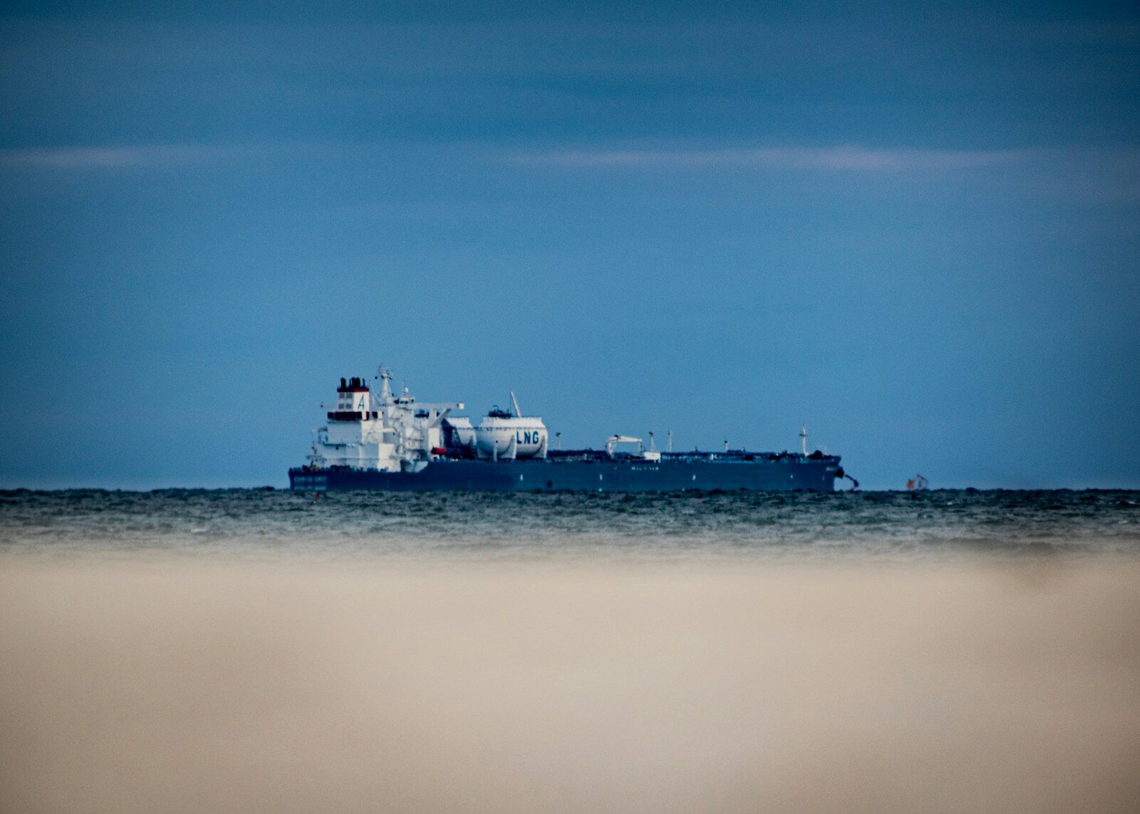 A large tanker on the horizon at dusk, seen across open water.