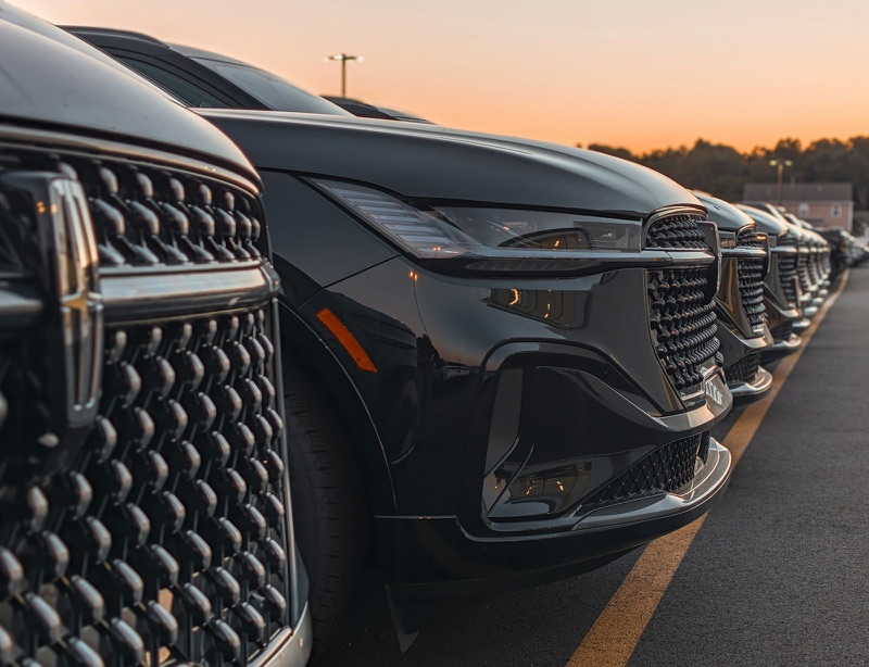 A row of new dark SUVs parked on a dealership lot at dusk.