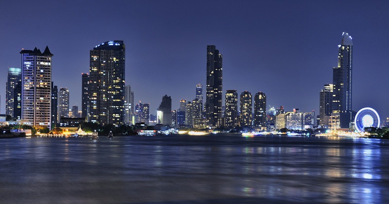 High-rise towers and a lit Ferris wheel along the Chao Phraya river in Bangkok at night.