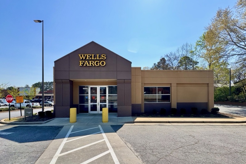A single-storey Wells Fargo bank branch with the company's gold lettering above the entrance, under a clear blue sky.