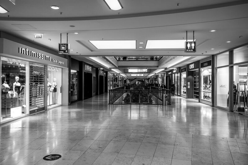 A largely empty shopping mall corridor lined with storefronts, in black and white.